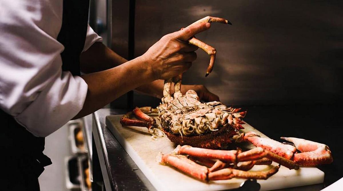 man preparing a large crab in a commercial kitchen.