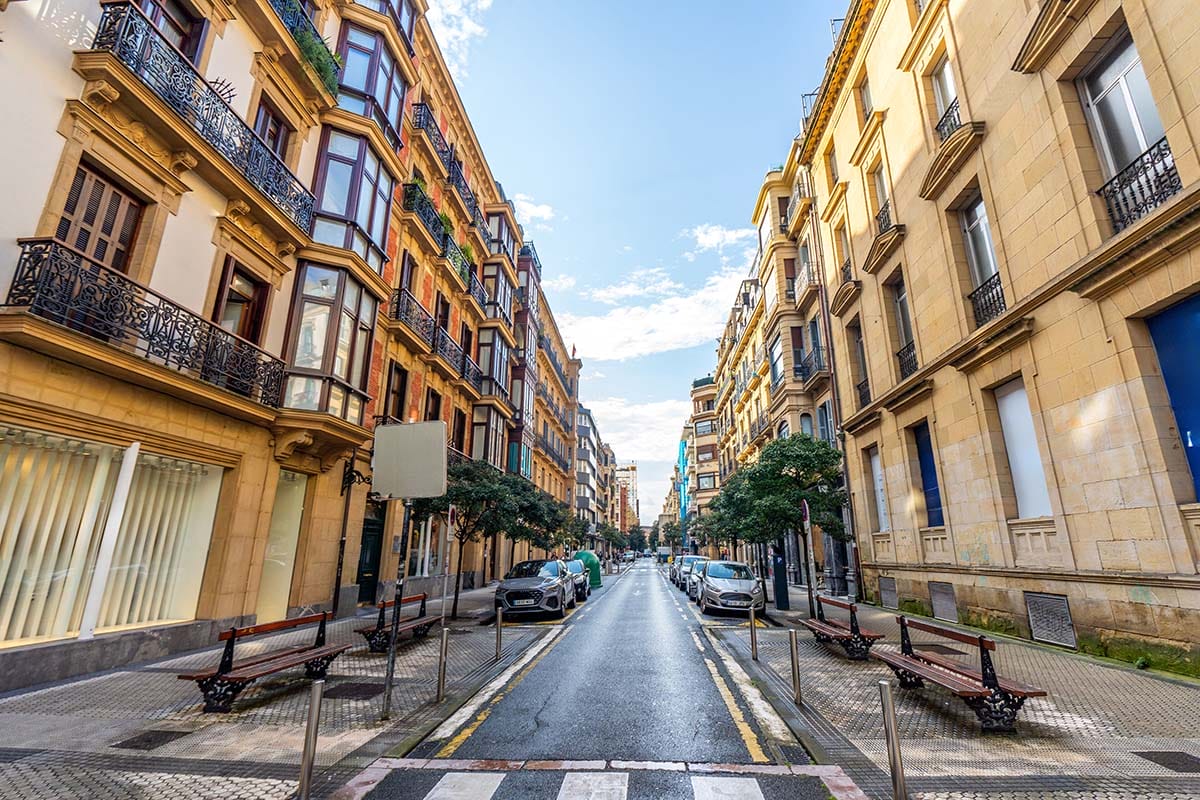 looking down a street with cars and benches beside multi-story buildings.