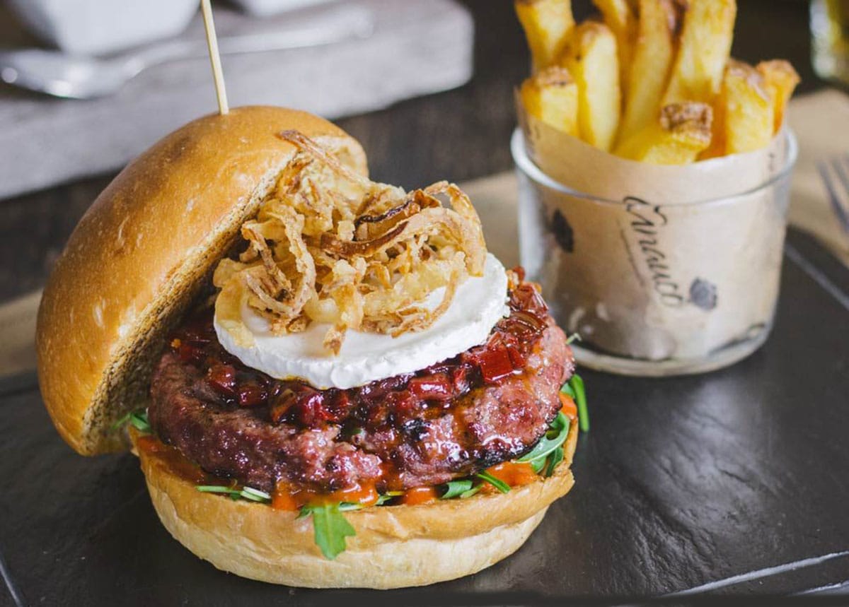 juicy burger on a toasted bun topped with fried onions and accompanied by French fries.