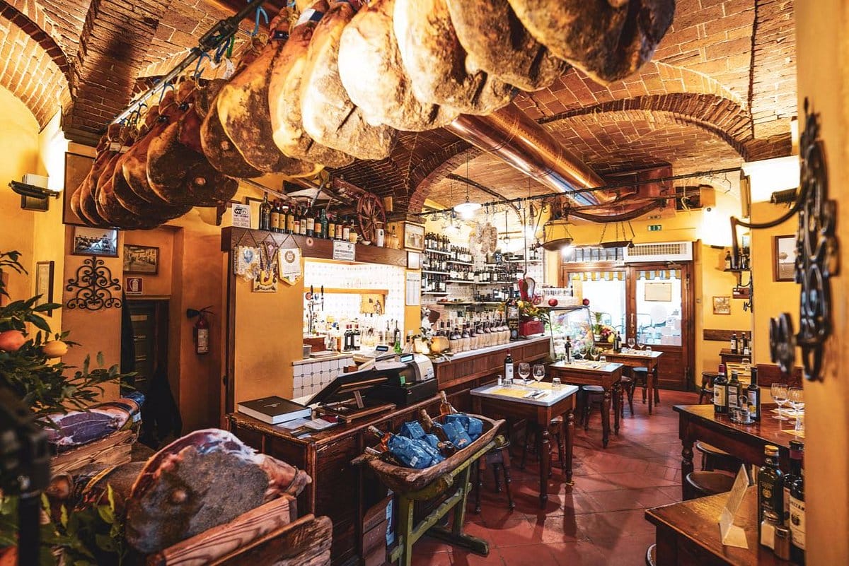 brick-ceilinged room with meat on display and a counter with many wine bottles behind it.