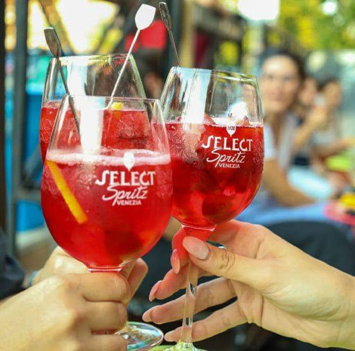 three people toasting with Aperol spritzes in glasses.