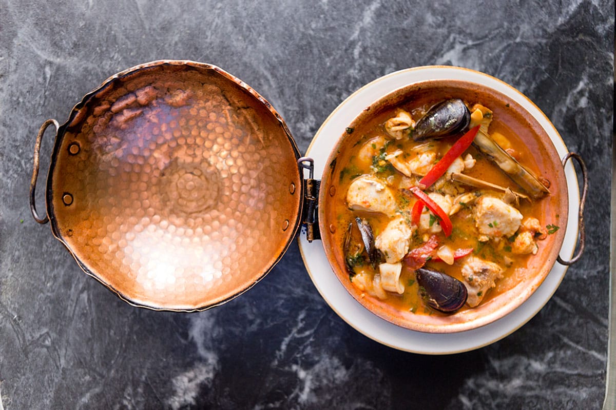 copper dish filled with seafood in a sauce.