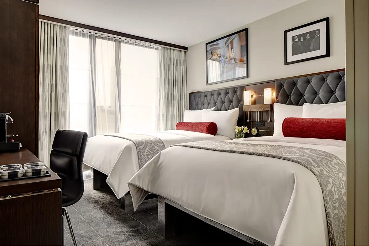 two double beds in a hotel room with framed artwork hanging on the wall above them.
