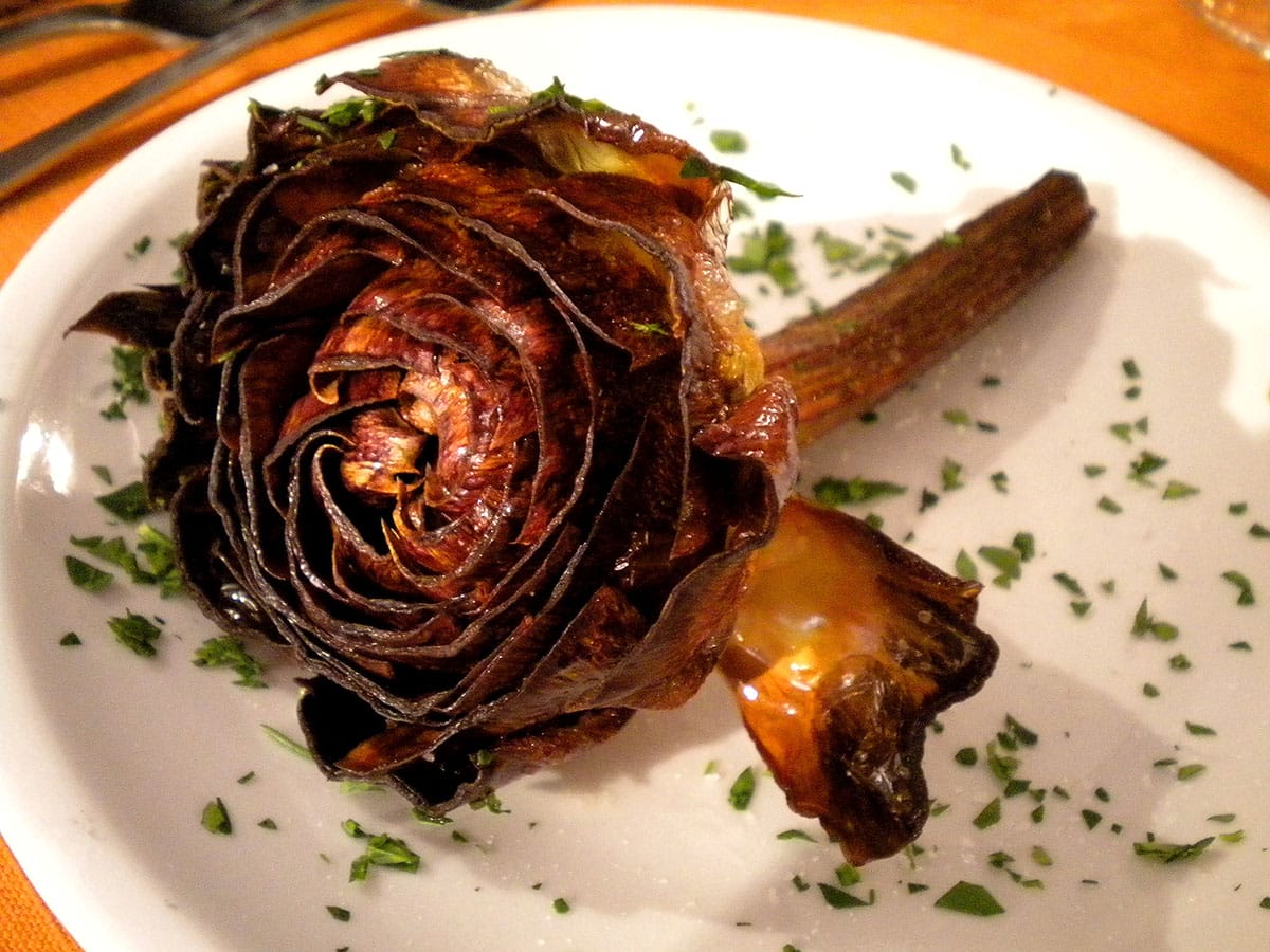 crispy artichoke sprinkled with herbs on a white plate.