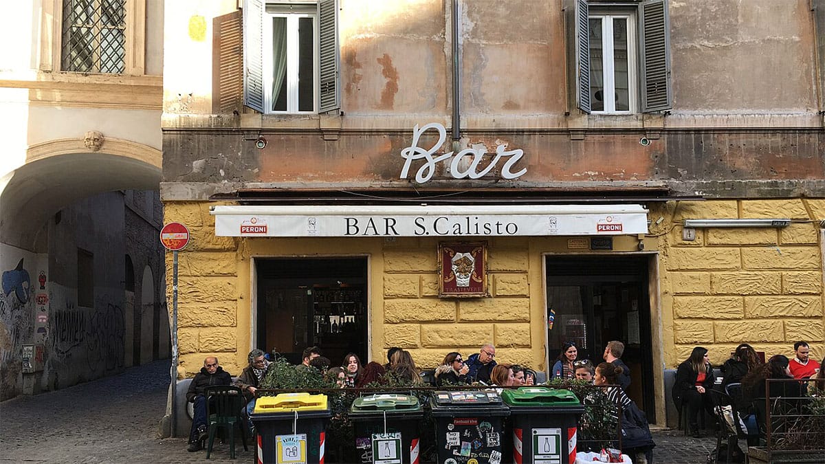 people sitting outside at tables outside of a Roman bar.