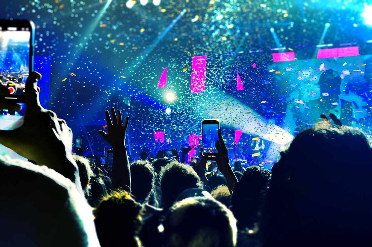 group of people at a concert with their hands in the air and videoing on cell phones.