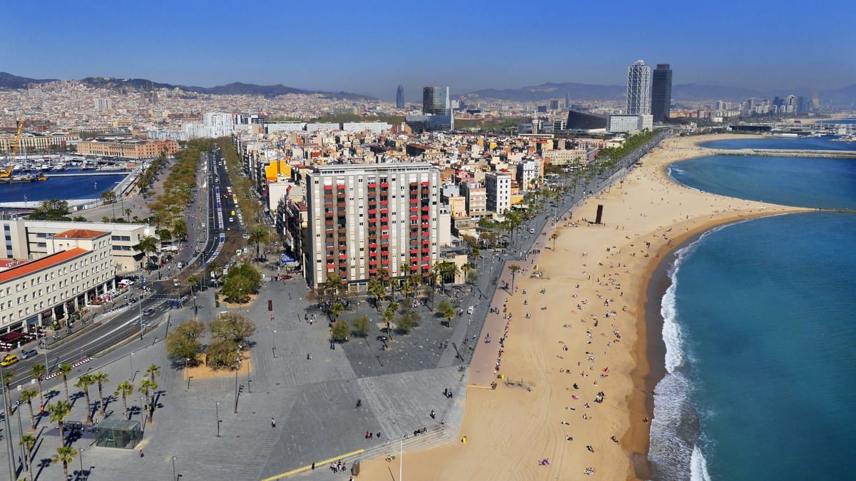 aerial view of a long, sandy beach near a city with a large parking lot nearby.