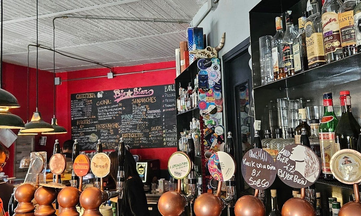 beer taps and walls of bottles at a bar with a chalkboard menu on the back wall.