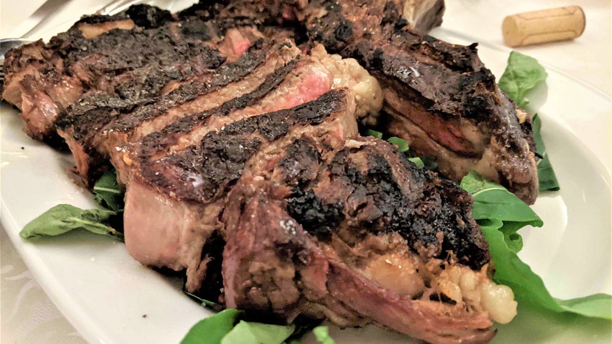 sliced medium-rare steak with greenery on a large white platter.