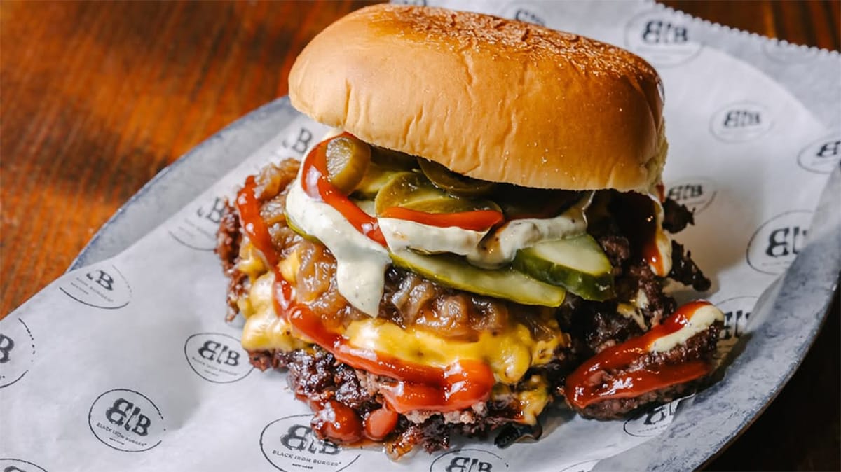 hamburger patty smothered in pickles and condiments on a tall bun.