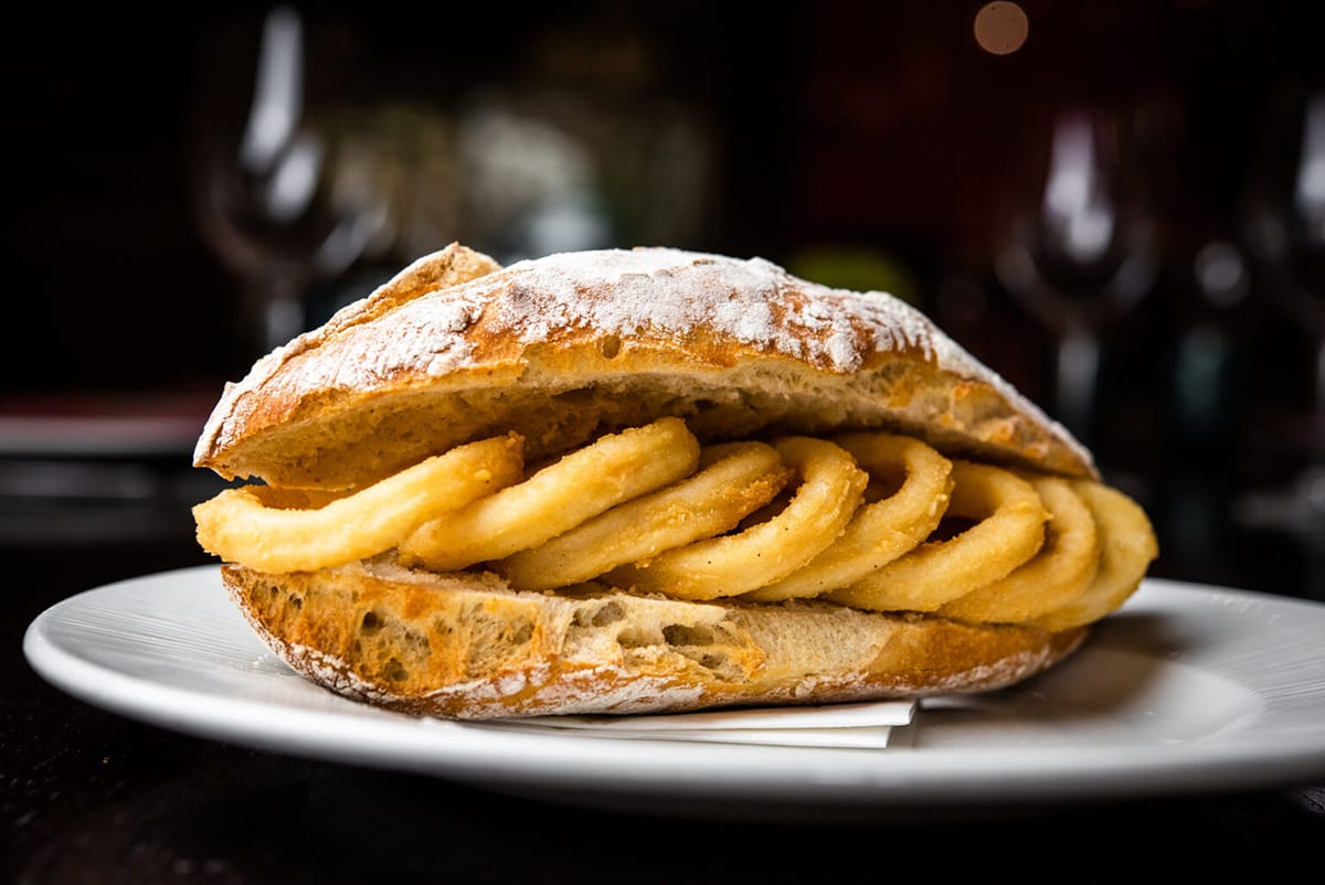 large fried calamari sandwich on a white plate.