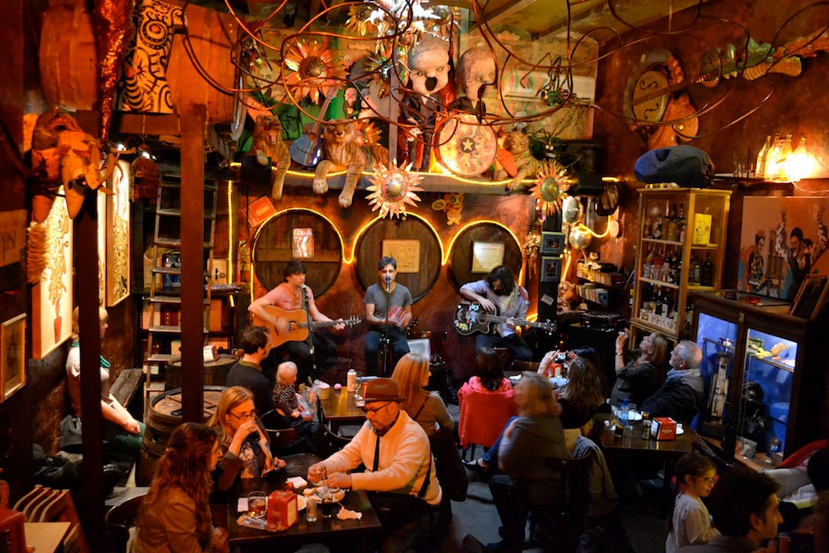 group of three musicians onstage with people sitting at tables and chairs nearby.