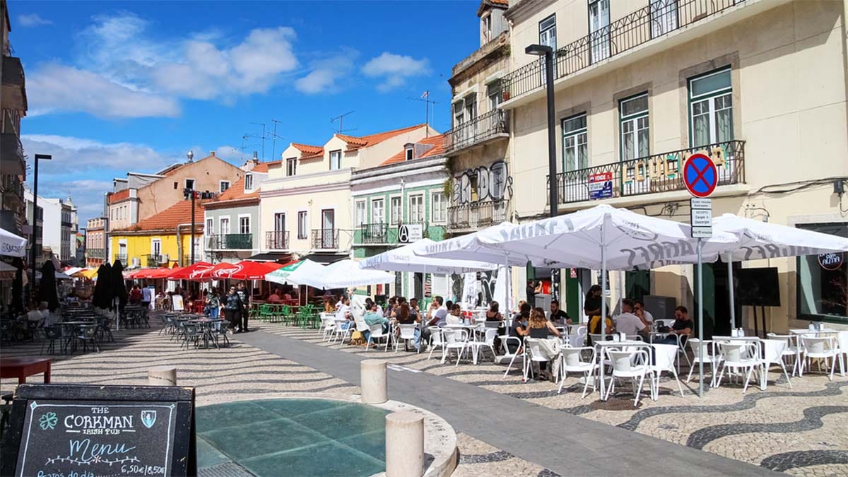 people eating outside on terraces under umbrellas near multi-story historical buildings.
