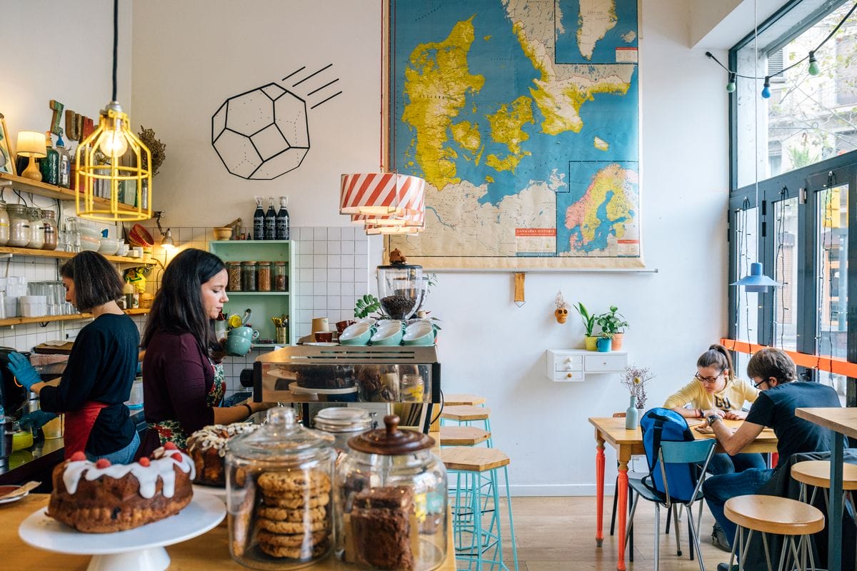 small coffee shop with tables and chairs with baked goods on the counter.