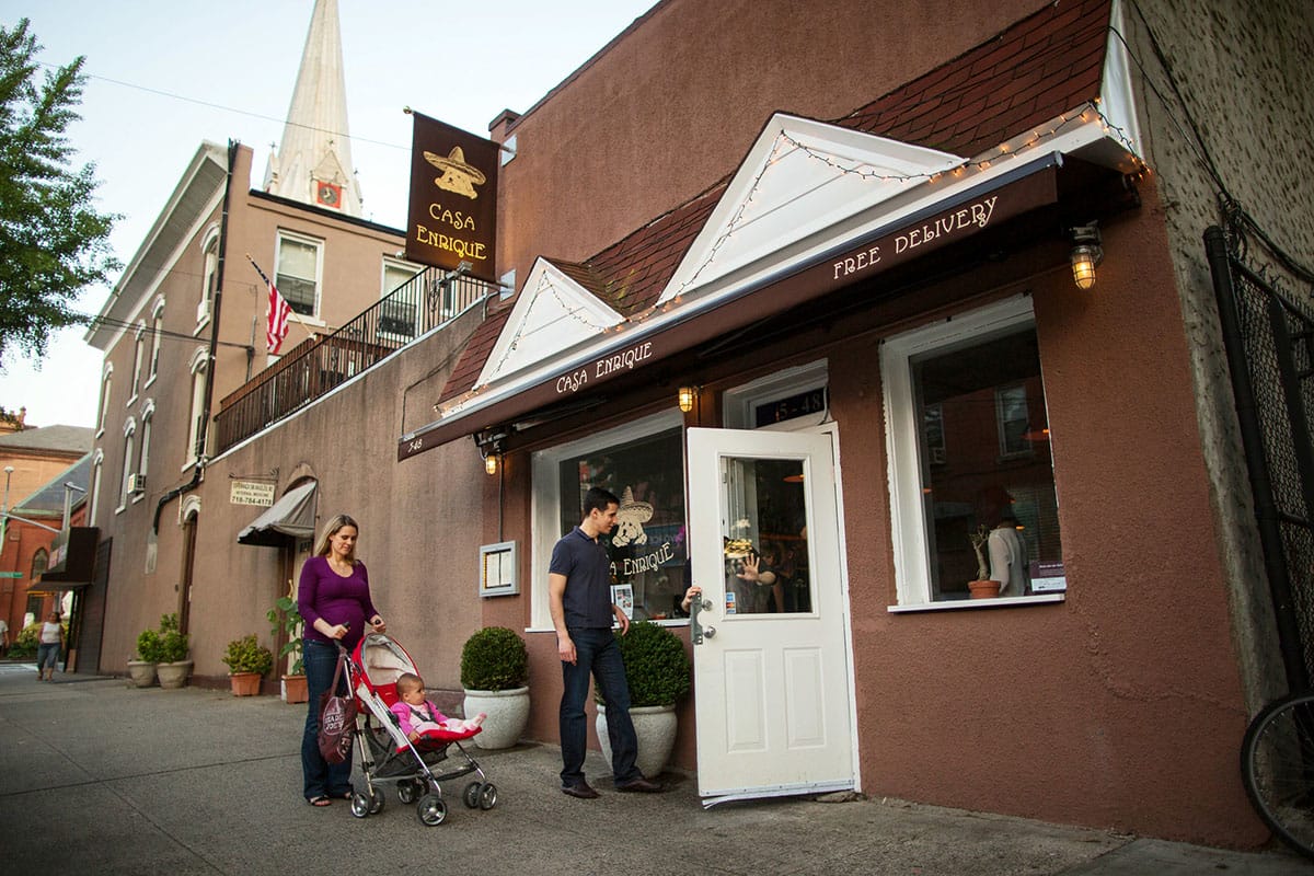 man and woman pushing a stroller with a small child as they enter a small brown-stucco building.