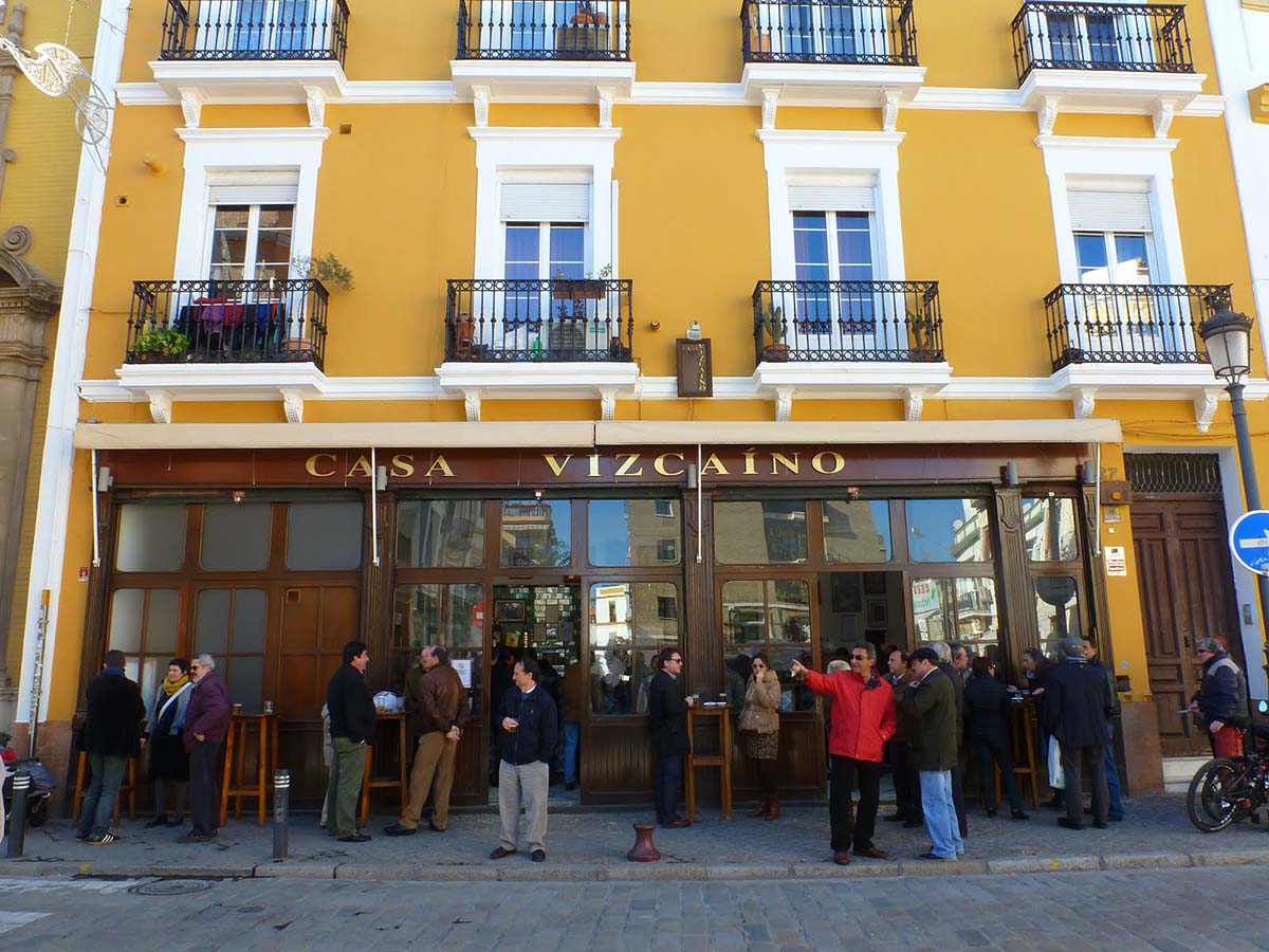 people standing on the sidewalk and eating and drinking at a tapas bar.