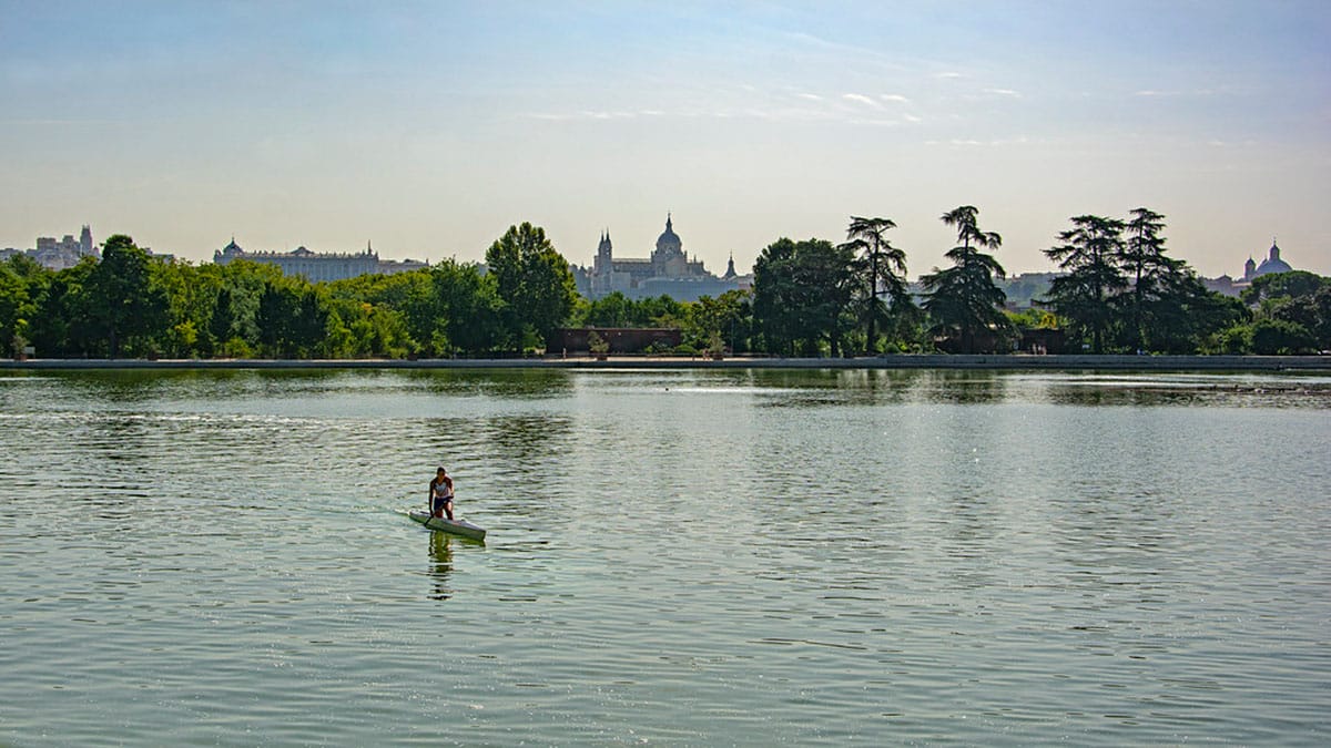 woman paddling a kayak on a tranquil pond with a castle in the background.