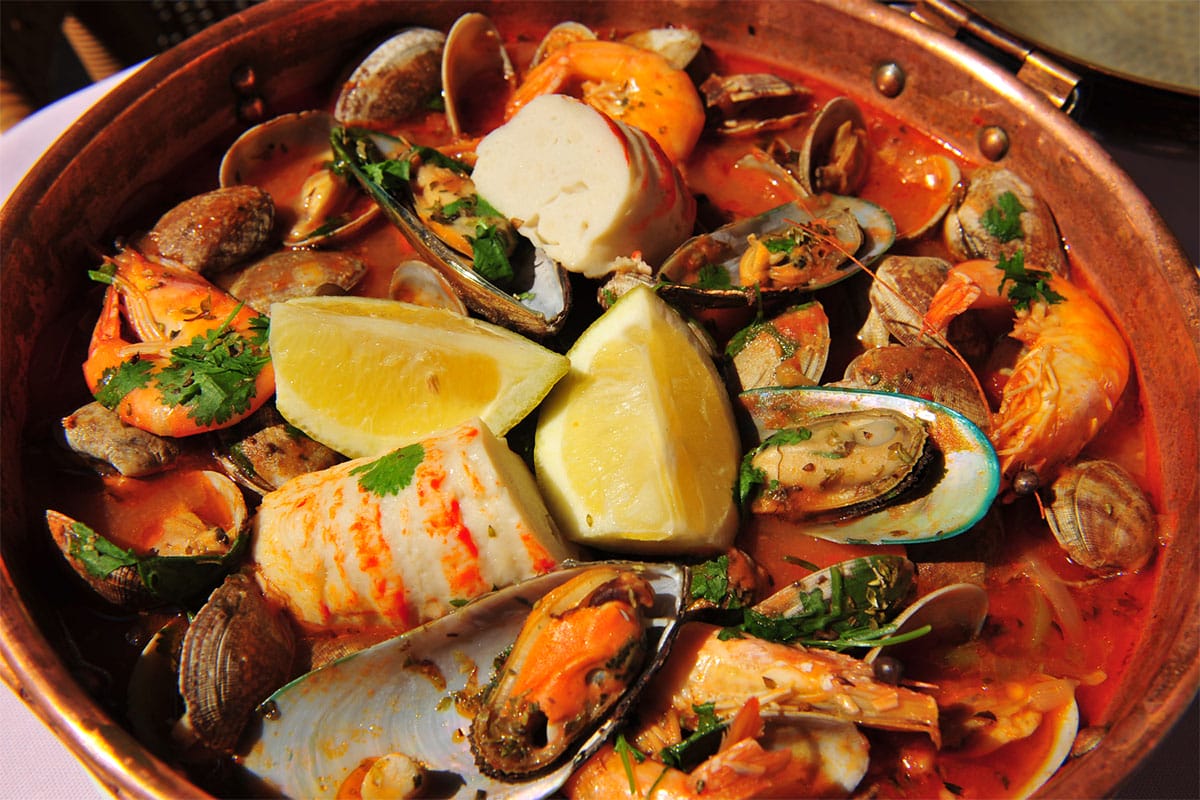 large copper stew pot full of seafood stew with fresh herbs.