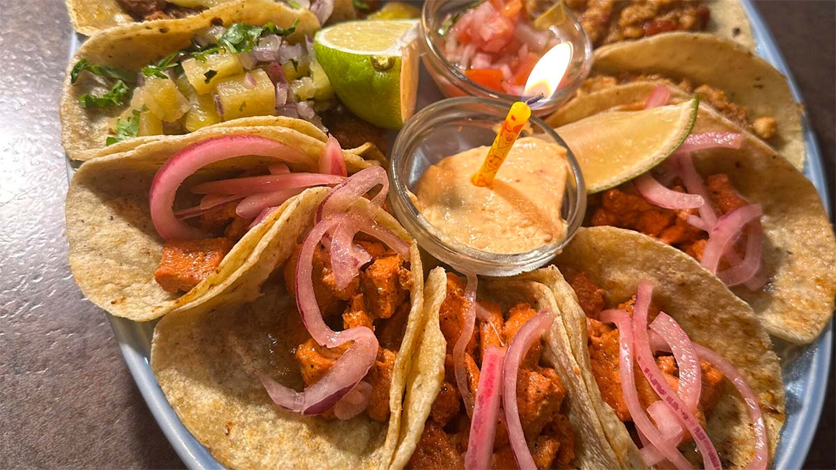 corn tortillas filled with different fillings along with a sauce and a lime wedge.