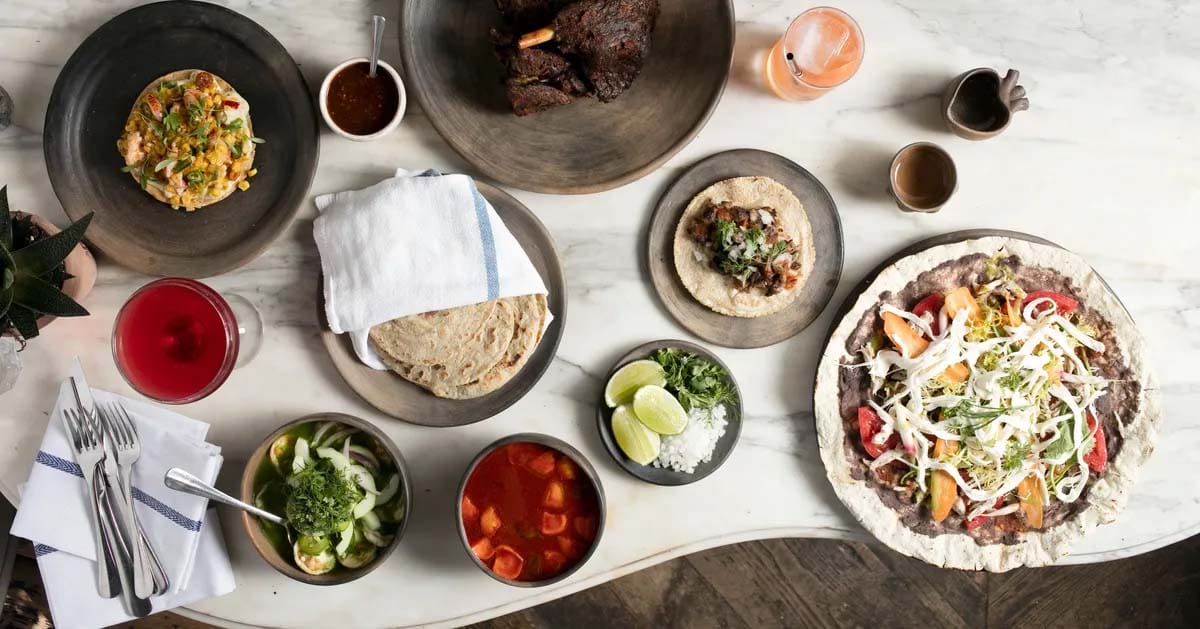 tortillas, toppings, and drinks on a marble-topped table.