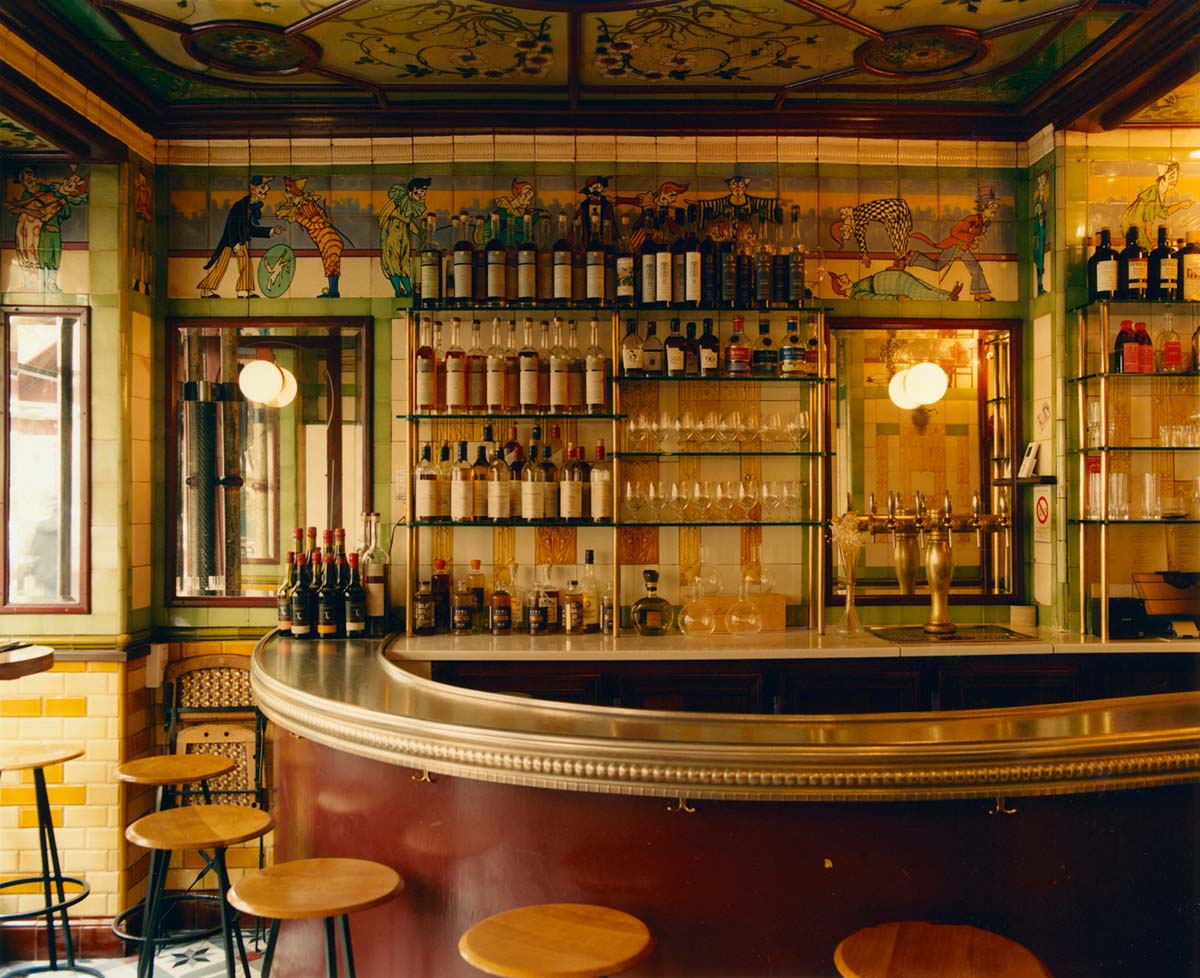 glass shelves of bottles and glasses in a tiled, warmly lit bar with an antique flair.