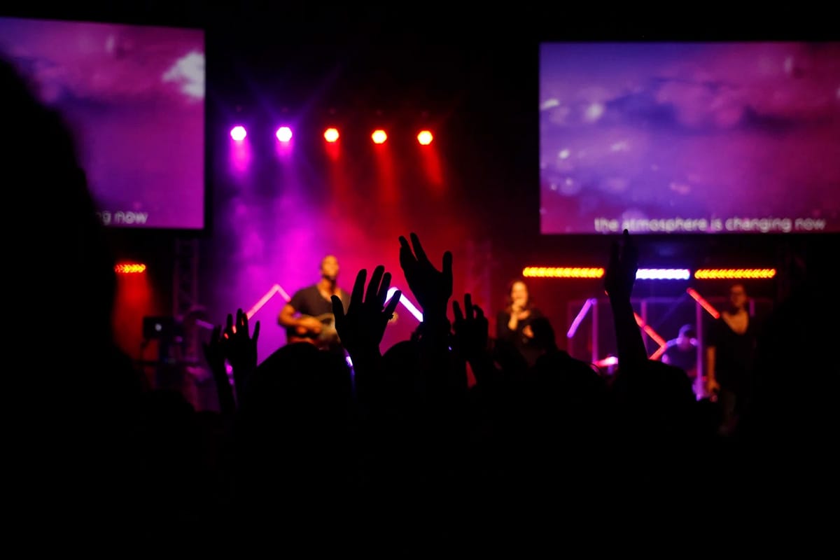 people with hands raised in a concert with pink and yellow lighting.