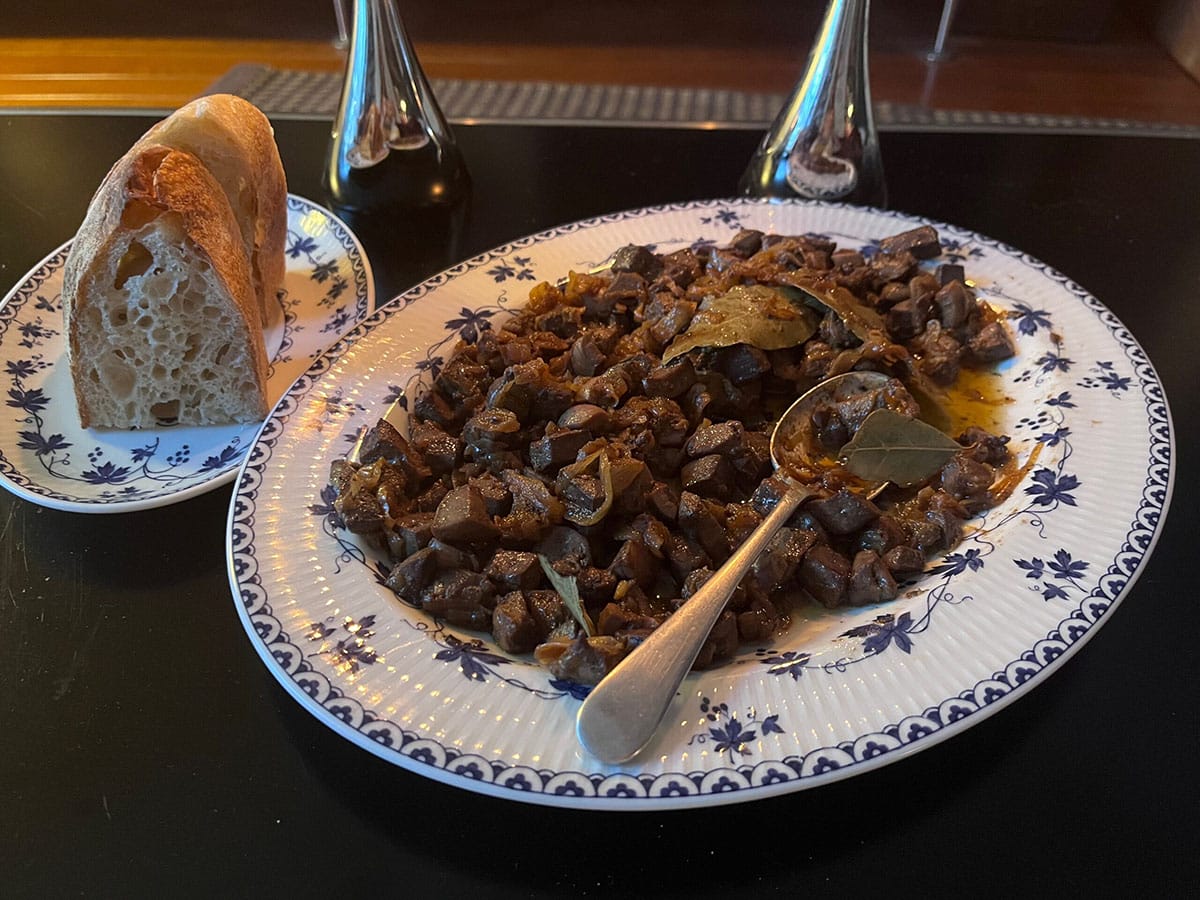 blue and white plate of coratella with a spoon and a smaller plate of sliced bread.