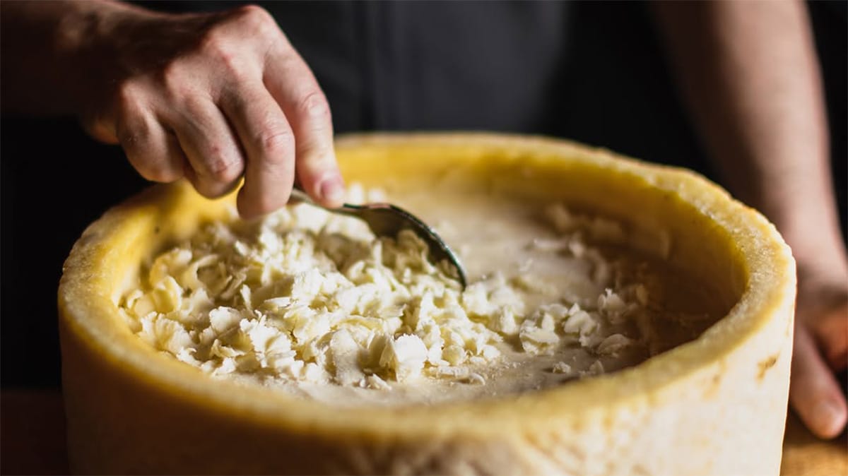 man tossing pasta in a hollowed-out wheel of Pecorino Romano.