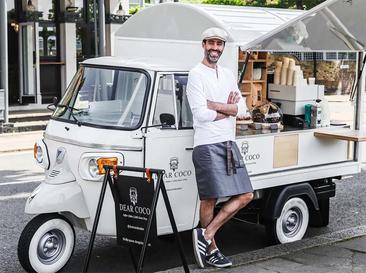man leaning on a small coffee truck.