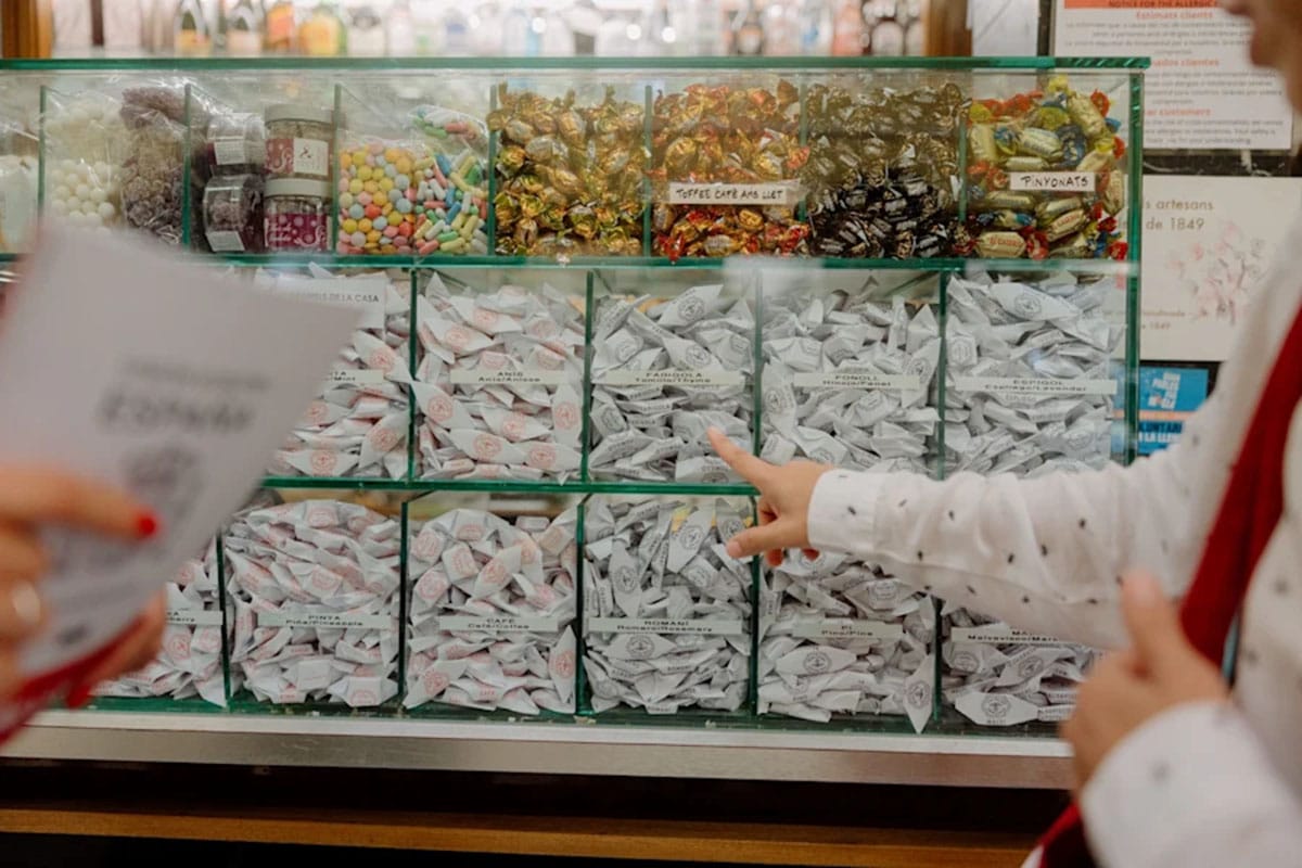 tour guide pointing to different individually wrapped candies in a glass display case.