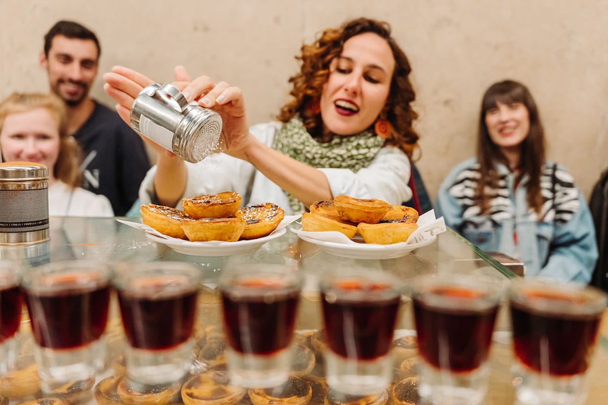 lady dusting pasteis de nata with powdered sugar.
