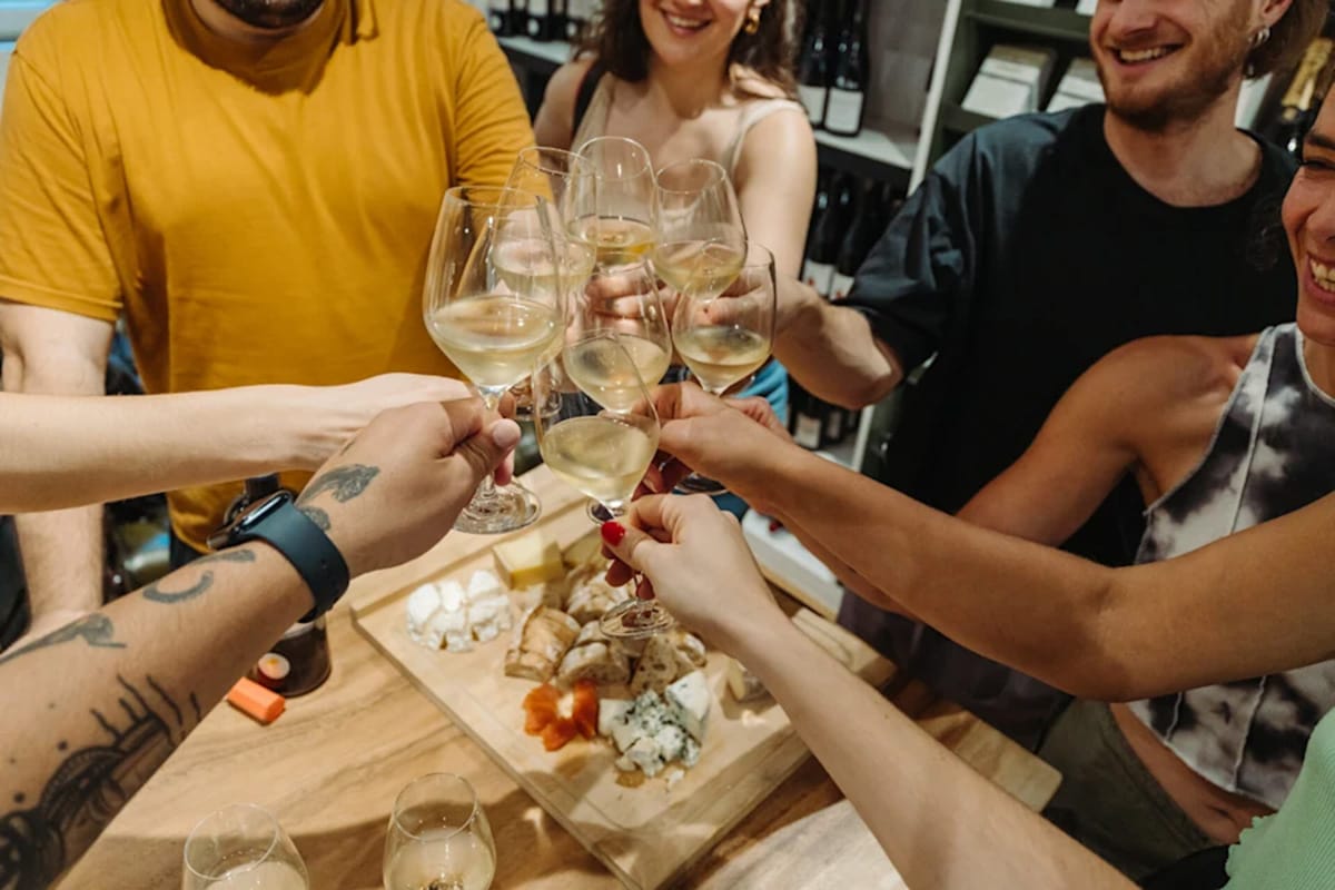 people toasting with glasses of white wine over a cheese board.