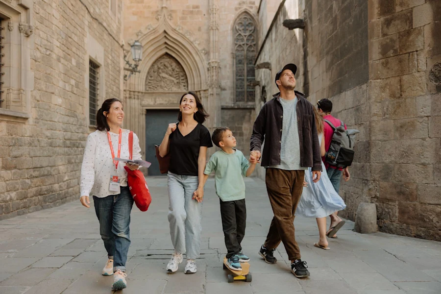 A family walks hand in hand with a guide through the Gothic Quarter, admiring the medieval buildings.