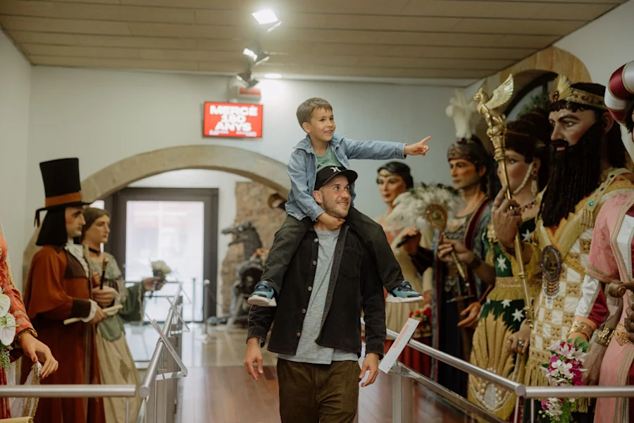 A boy sits on his father’s shoulders while pointing excitedly at giant festive figures inside a museum.