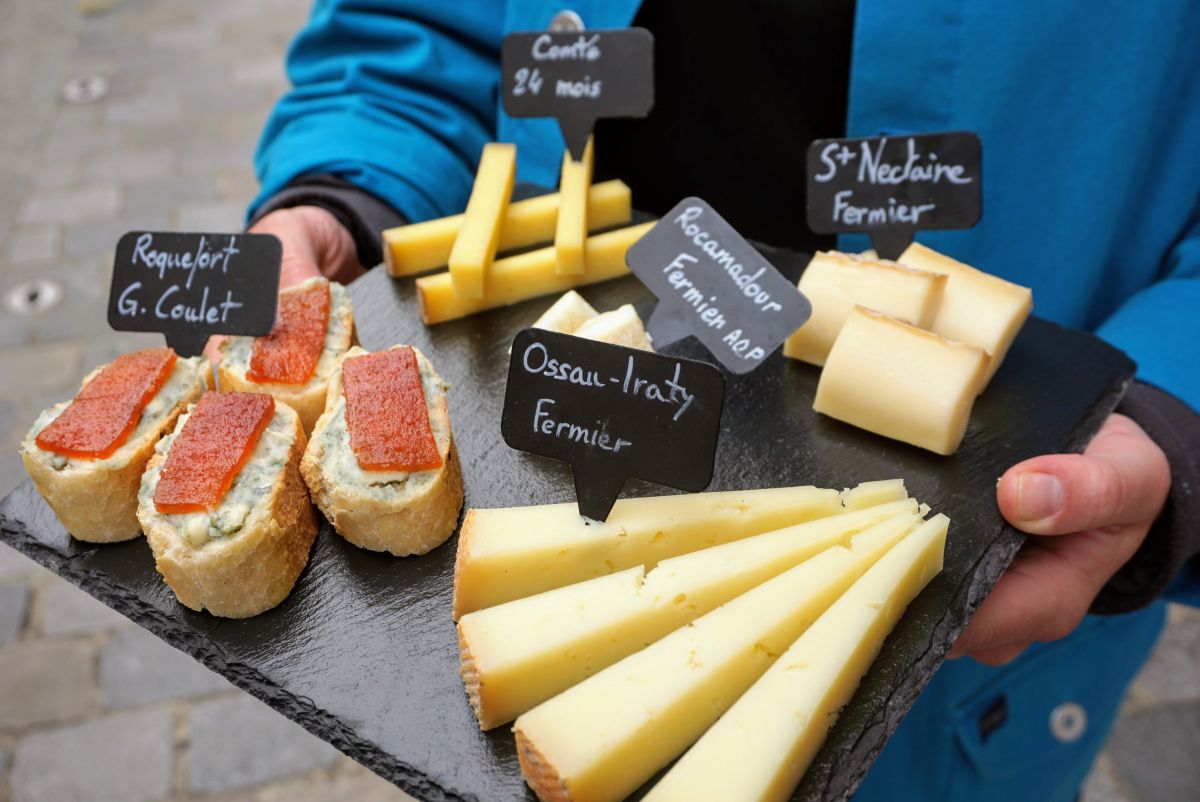 A woman holding a platter with an array of French cheeses.
