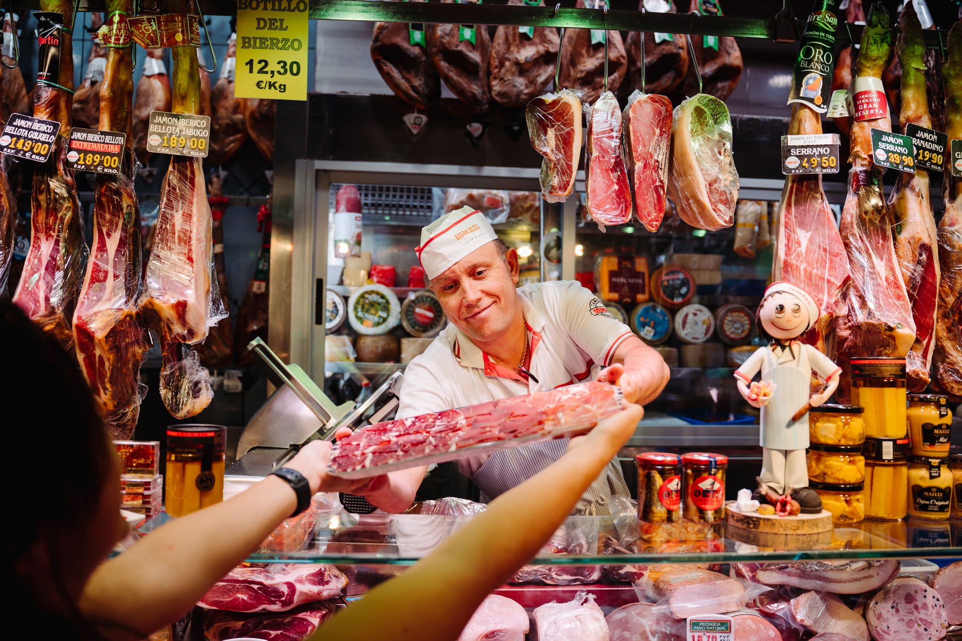 market owner handing a platter of cured hams to a lady.