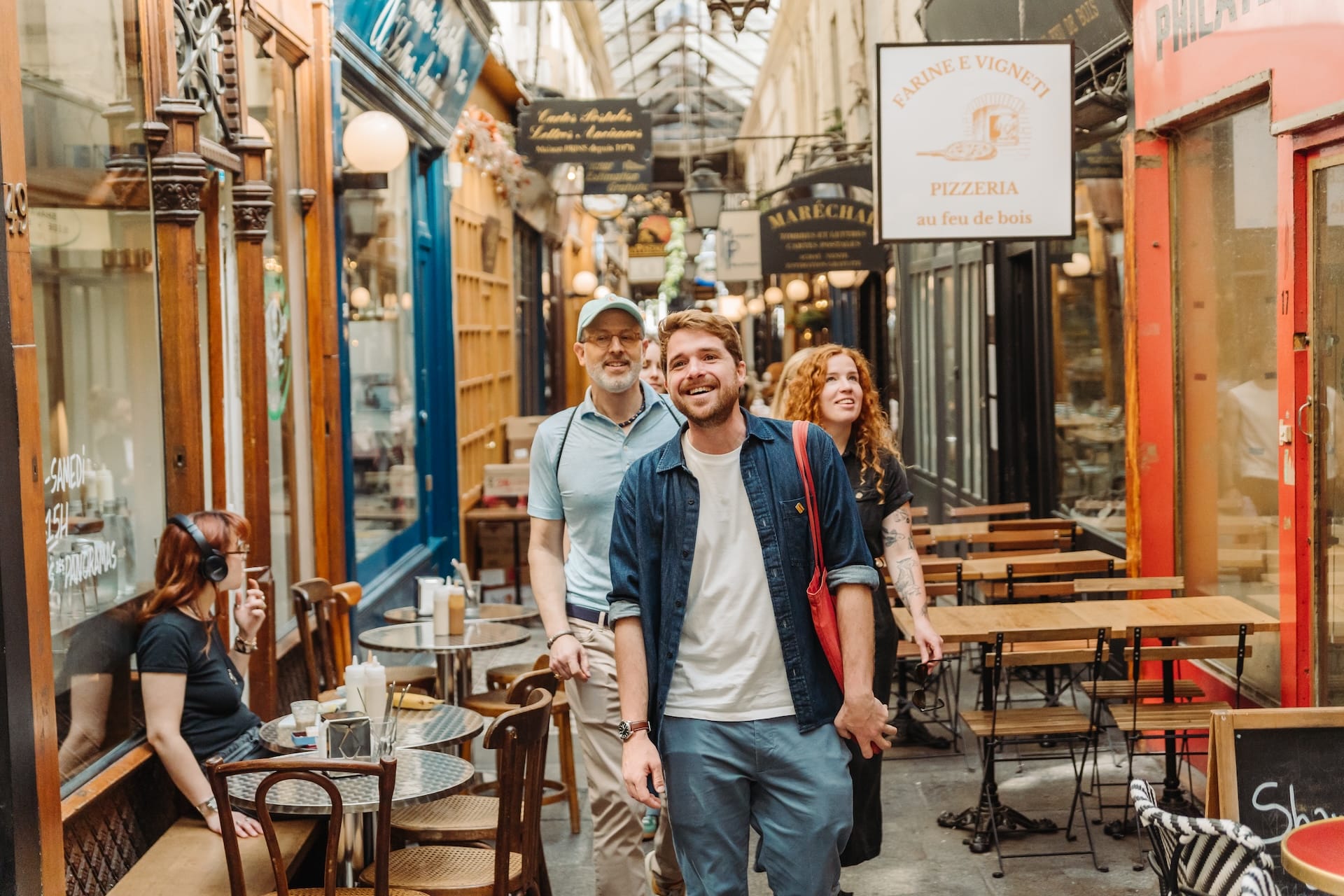 A small group of people walking through a charming covered alleyway filled with cafés and restaurant signs. They appear to be enjoying the stroll, smiling and taking in the surroundings.