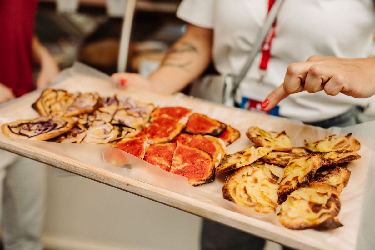 person holding a board of bread with various toppings.