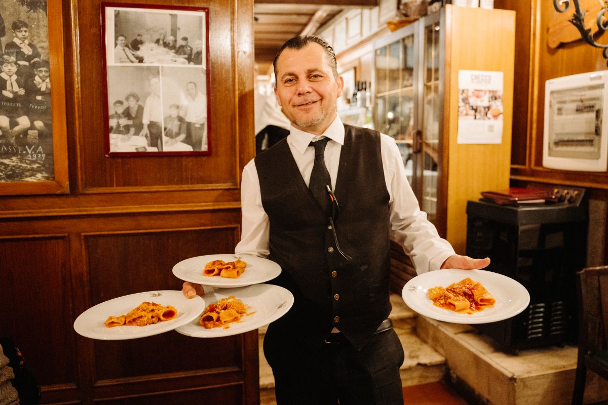 A waiter holding plates of rigatoni with a tomato-laden oxtail sauce and coda alla vaccinara.