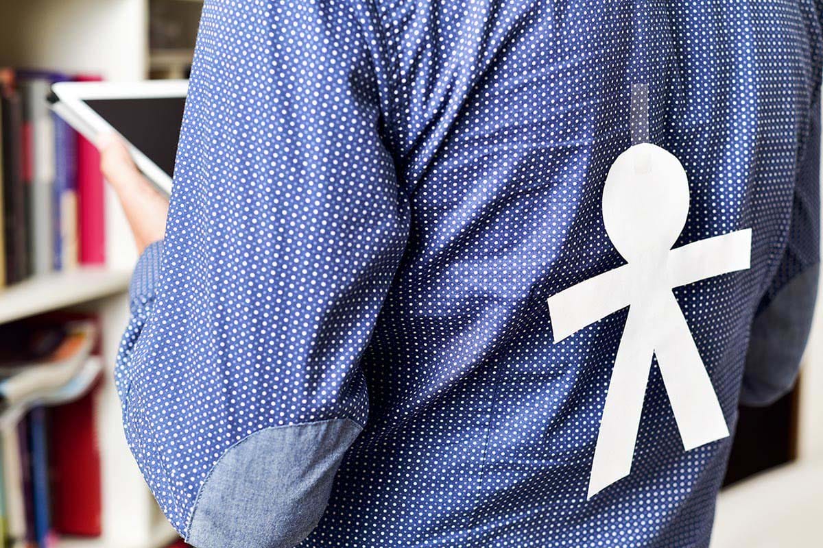 white paper doll taped to the back of a man's shirt.