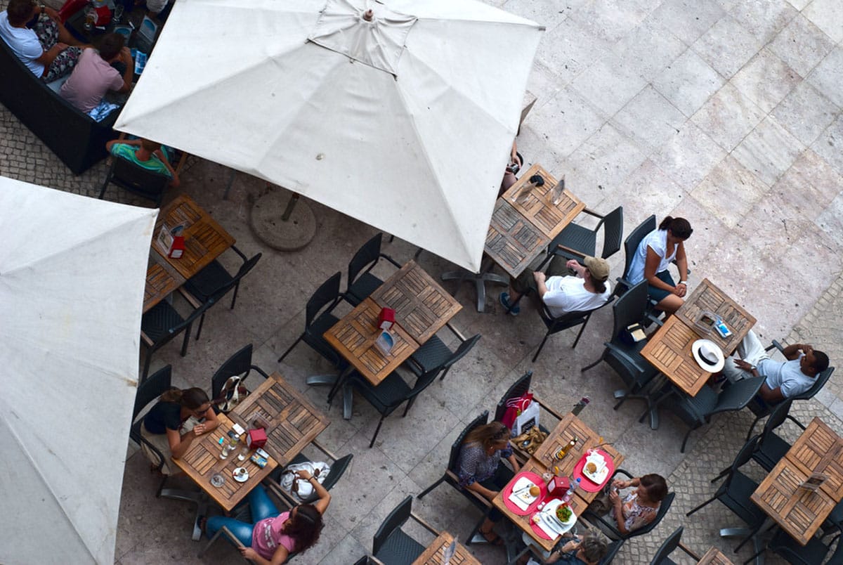 people sitting at tables eating lunch with large umbrellas over their heads.