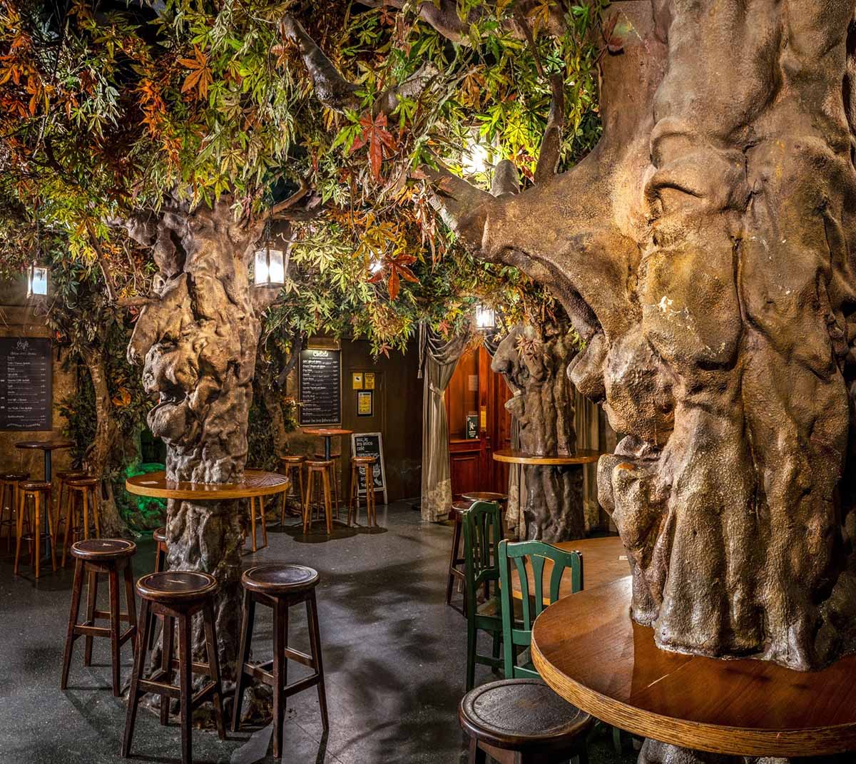 tables and bar stools around artificial indoor trees with foliage and lighting.