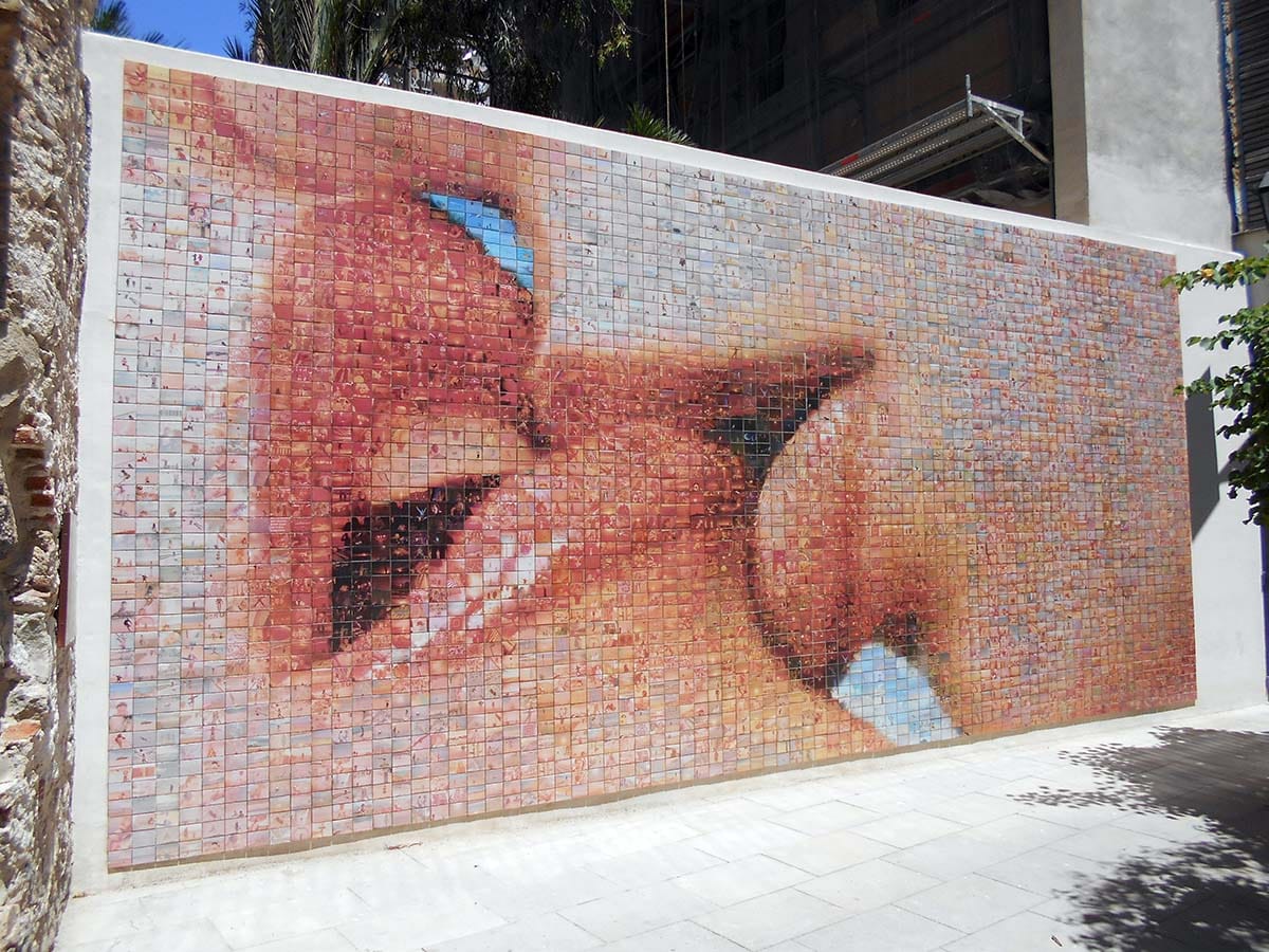 mosaic of a kiss made from photographs on a wall outdoors.