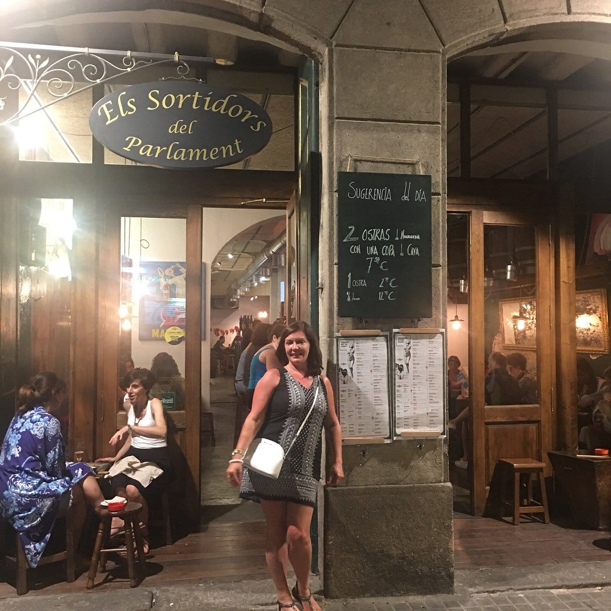 woman smiling and standing beside a menu board outside of a restaurant in Barcelona.