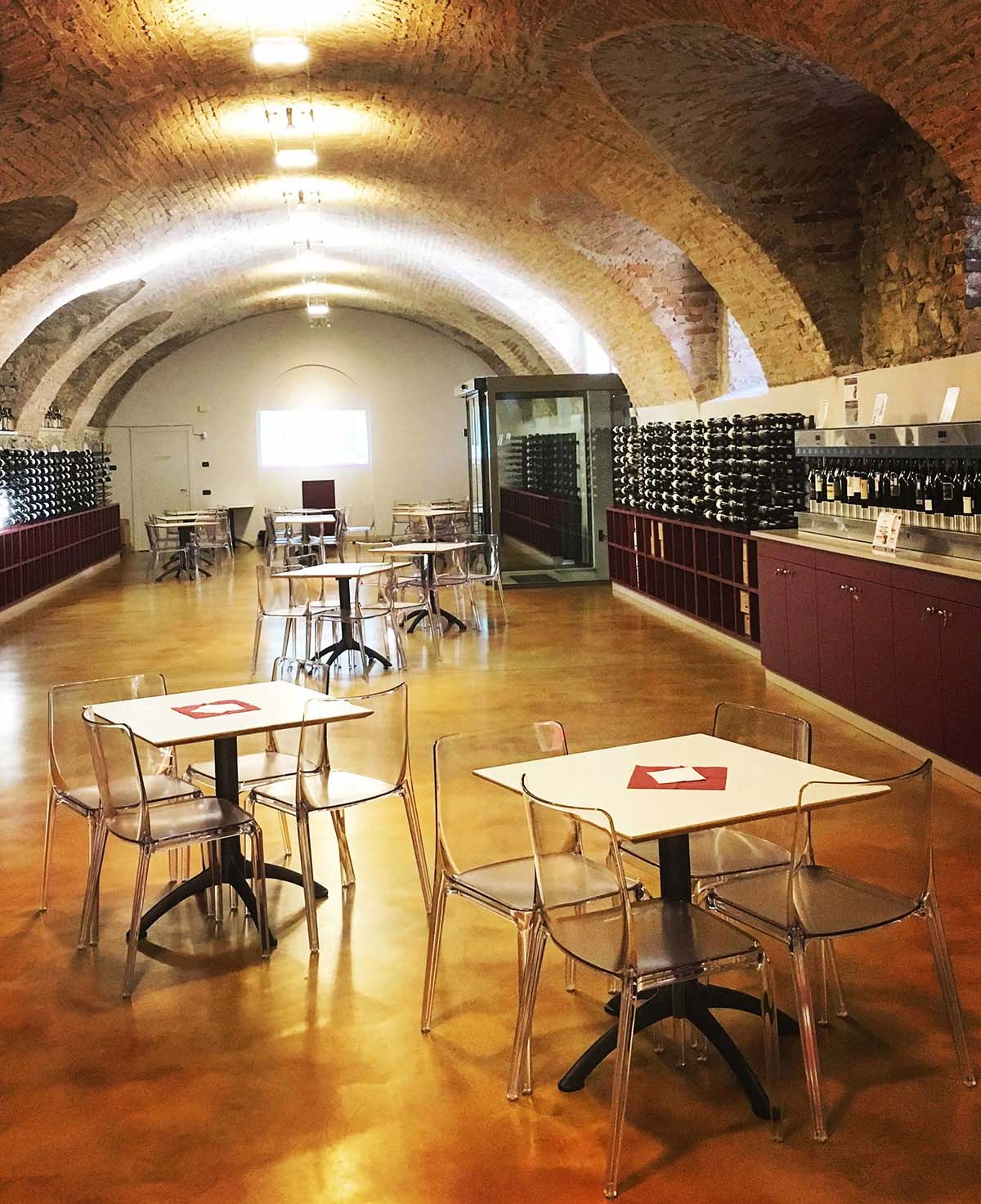 tables and chairs in an underground wine cellar with wine bottles on shelves.
