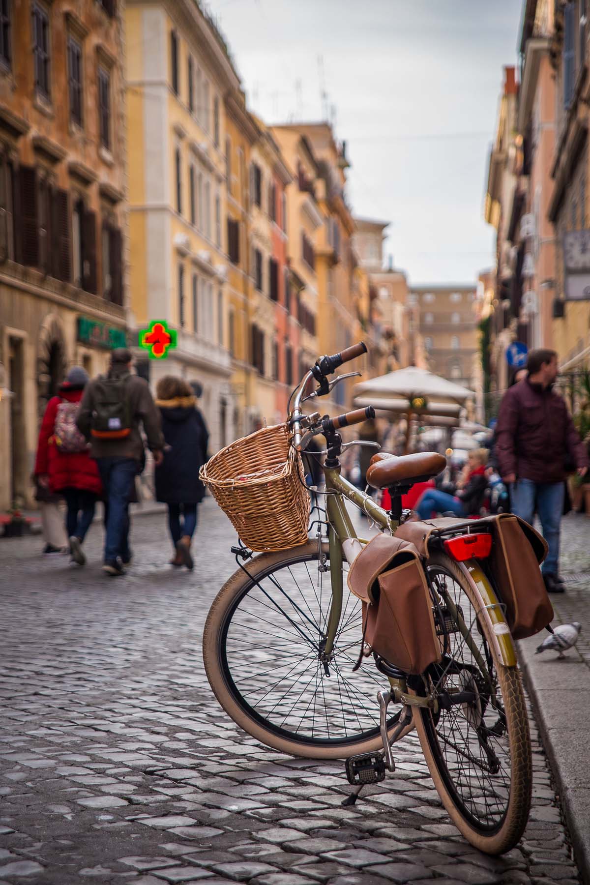 bike with a wicker basket on the handlebar parked at the curb of a cobblestone street.