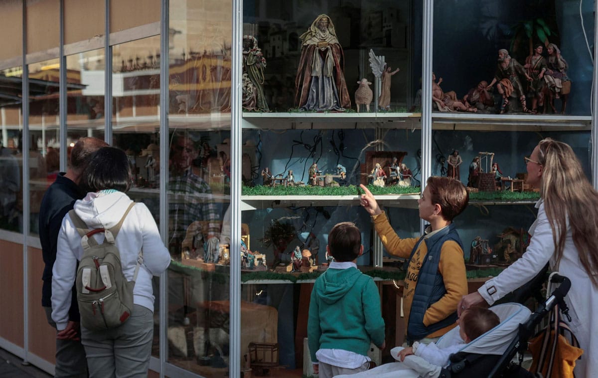 a man, woman, and children looking at Nativity figures on shelves.