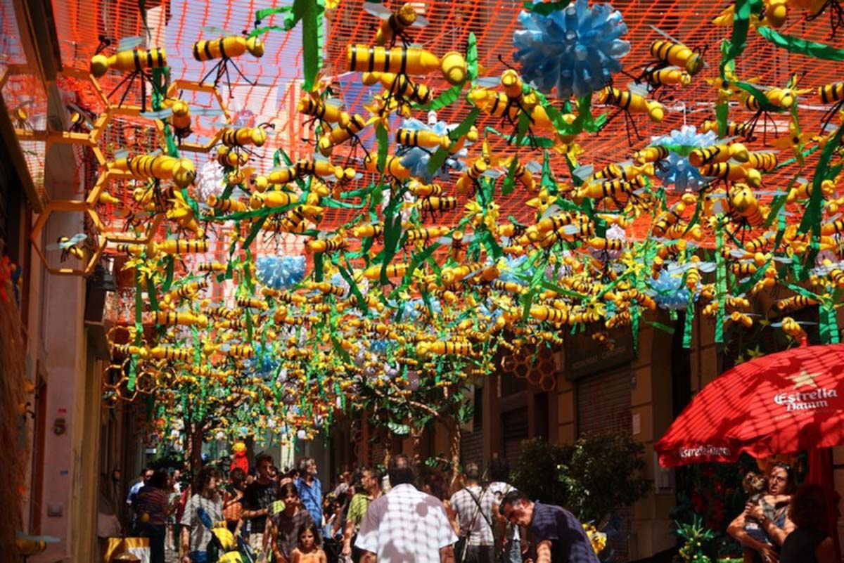 mesh hanging over the street with bumblebee and flower decorations with people walking underneath.