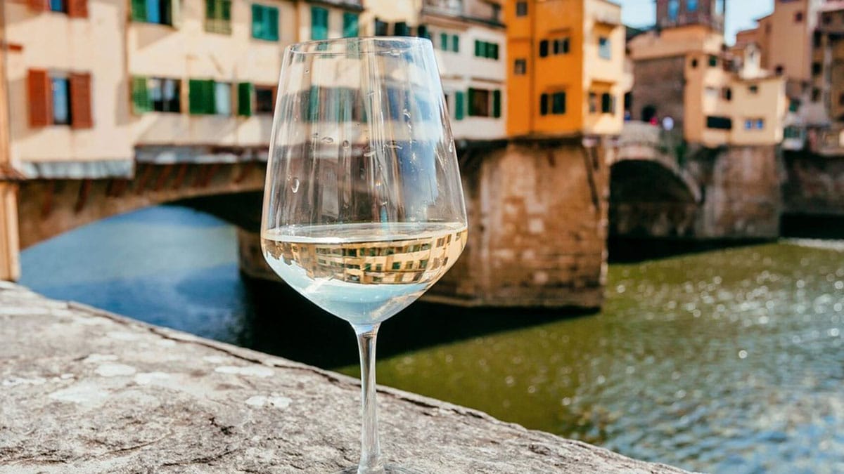 glass of white wine on a stone railing overlooking a river in Florence.