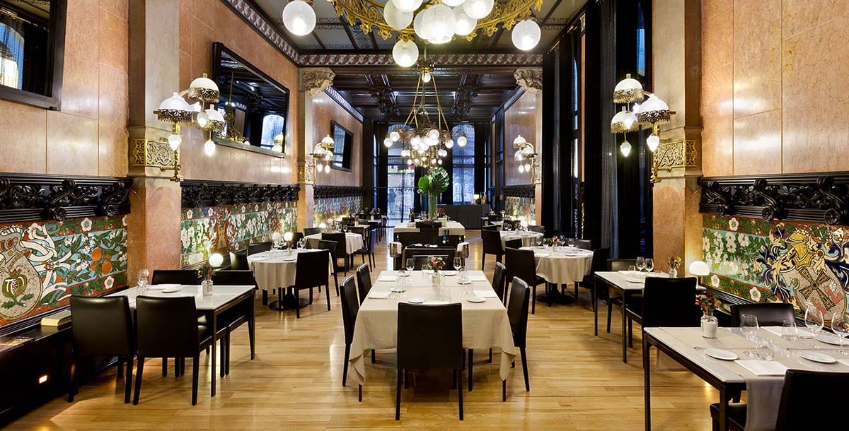 tables and chairs in a long, high-ceilinged room illuminated with round chandeliers.